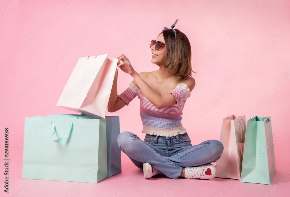 Fototapeta premium Asian pretty young woman walking over pink pastel background. She smiling and holding shopping bags. she nice-looking lovely attractive shine .