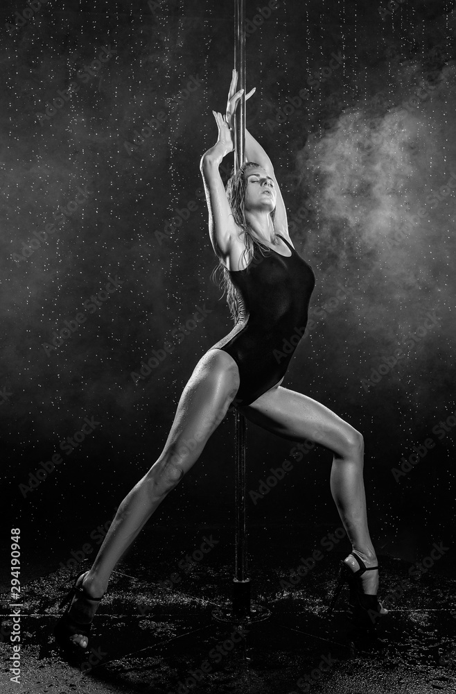 Beautiful wet athletic busty elegant blonde girl performs artistic elements of an exotic dance on the rain in a theatrical smoke. Health, lifestyle, sports black white monochrome design. Copy space.