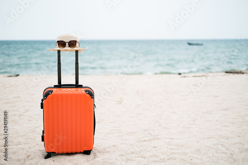Summer holiday and traveler concept  Straw hat with sunglasses is on the orange suitcase on the beach and sea background with copy space