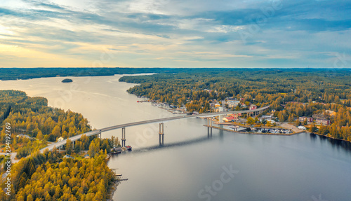 Aerial view on the bridge over the lake and trees in the forest on the shore. Blue lakes, islands and autumn forests from above on a cloudy summer day. Lake landscape in Finland, Puumala. photo