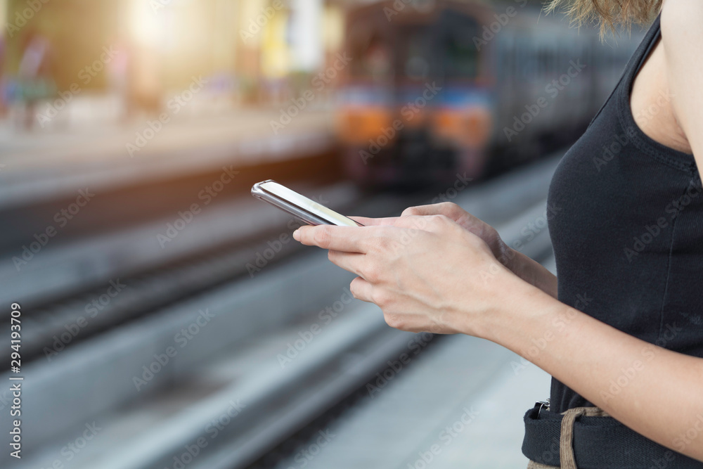 Woman standing and waiting for train and using smart phone in train station. Travel concept. Woman standing and waiting for train and using smart phone in train station. Travel concept.