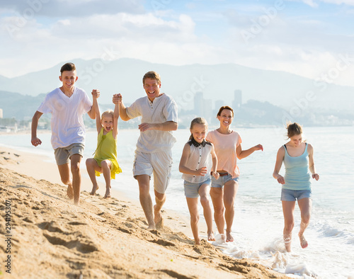 Family of six people happily running together on beach