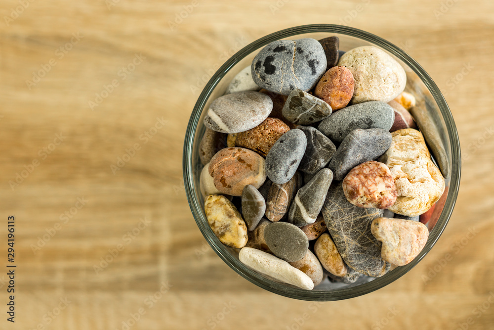Small sea stones in a glass vessel. The idea of decorating the house with small  rocks in a jar on a wooden blurred background. Stock Photo