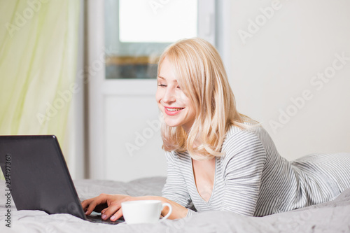 Pretty woman using laptop while having a cup of coffee on bed