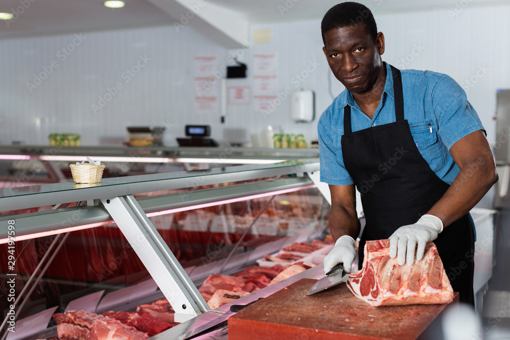 Confident African American male butcher cutting fresh meat in butcher shop