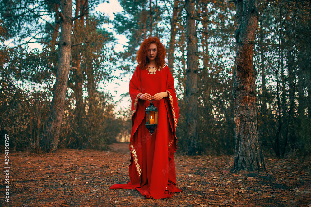 Woman in red holding a lantern with a candle. Hand lantern with a candle shines in the woods. Woman in red holding a lantern with a candle. Hand lantern with a candle shines in the woods.