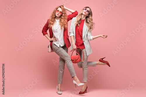 Fashionable autumn woman with stylish hairstyle, makeup dance. Two Shapely blonde redhead girl having fun, trendy red outfit, heels, fashion hair, make up. Excited model, autumnal beauty pink concept