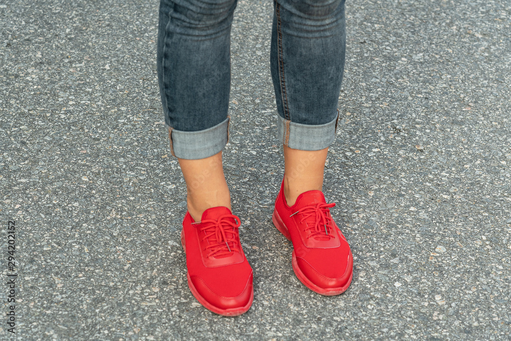 Female legs in red sneakers and jeans pants. Leather sport wear.