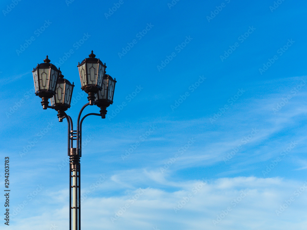 Vintage style city lantern in the street against a blue sky with clouds