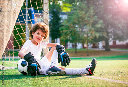 Smiling boy with bending arm on football sitting. Little boy plays football on stadium © kravik93