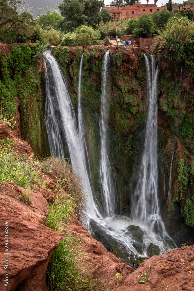 A view from the top of waterfall surrounded with green grass and orang colour terrain, Ouzoud Falls. Moyen Atlas village of Tanaghmeilt, Atlas mountains, Morocco.