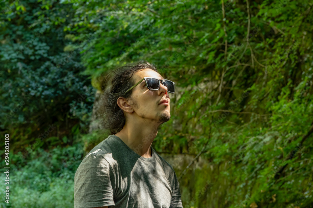 Walk outdoors. A young man in sunglasses looks at the nature around him. Sunlight falls on the face. Walk outdoors. A young man in sunglasses looks at the nature around him. Sunlight falls on the face.