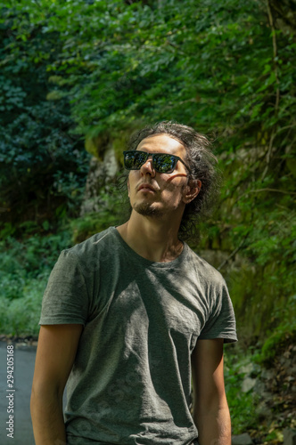 Walk outdoors. A young man in sunglasses looks at the nature around him. Sunlight falls on the face.