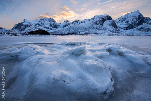 Beautiful landscape cracking ice, frozen sea coast with mountain ridge background at sunset in Lofoten Islands, winter season, Norway