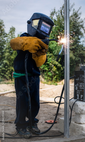 A child, a boy pretends to weld a fence. Welder's costume, gloves, mask.