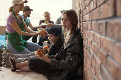 Принти на полотні Teenage girl with other poor people receiving food from volunteers indoors