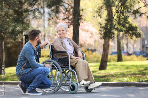 Senior woman in wheelchair with young man at park photo