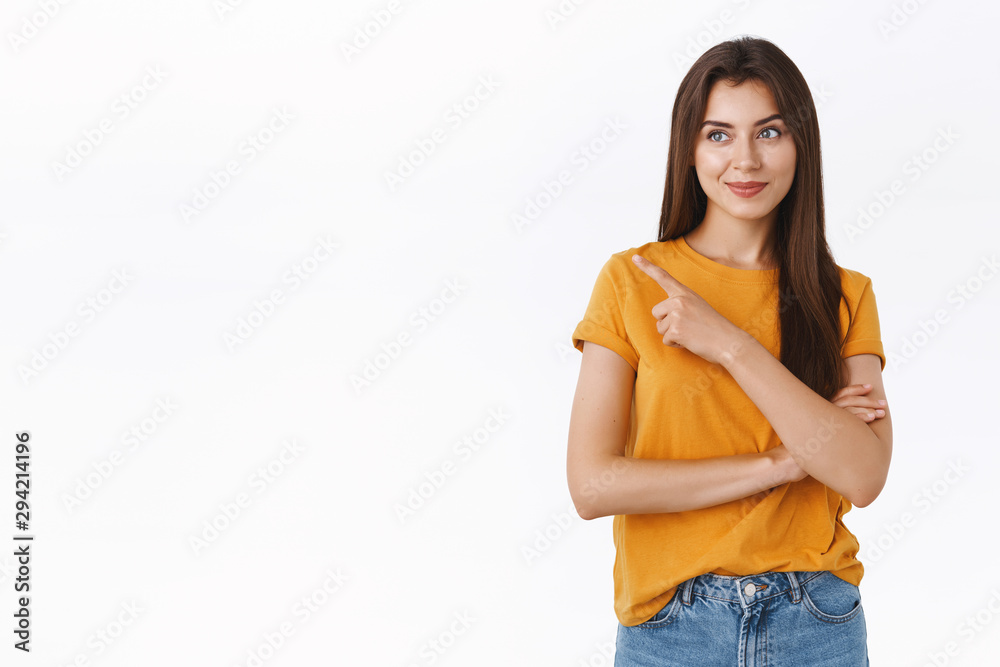 Smiling happy and pleased good-looking caucasian woman in yellow t-shirt made her choice, pointing and gazing upper left corner with satisfied grin, standing white background delighted