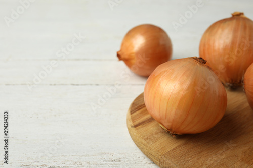 Board with ripe onions on white wooden table  space for text