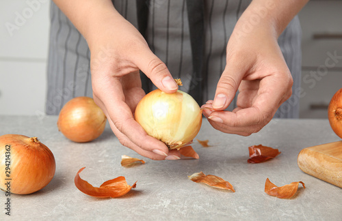 Young woman peeling ripe onion at grey table, closeup