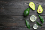 Bowls of natural oil and avocados on black wooden background, flat lay. Space for text