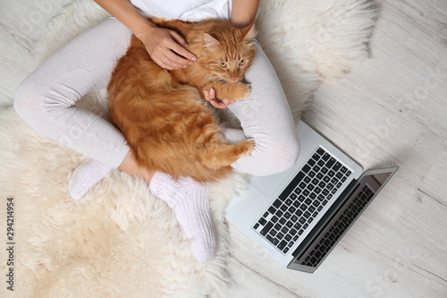 Woman with cute red cat and laptop on fur carpet, top view
