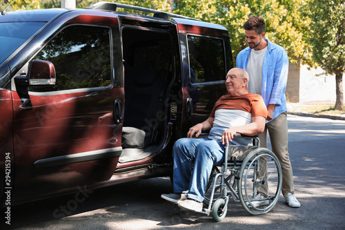 Young man helping patient in wheelchair to get into van outdoors