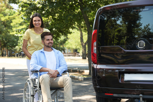 Young woman with man in wheelchair near van outdoors