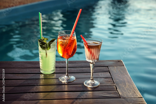 Photography Glasses of fresh summer cocktails on wooden table near swimming pool outdoors