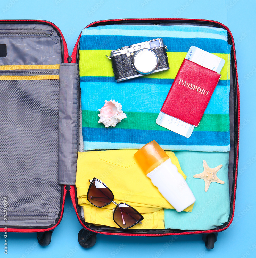 Naklejka premium Open suitcase with beach objects on blue background, top view