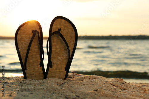 Stylish flip flops on sand near sea  space for text. Beach accessories