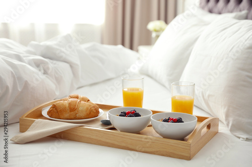 Tray with tasty breakfast on bed in light room