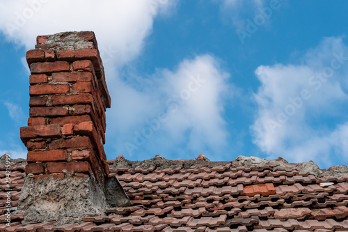 Canvas Print Old red terracotta tile roof with a damaged traditional large brick chimney in need of repair, on a blue sky background