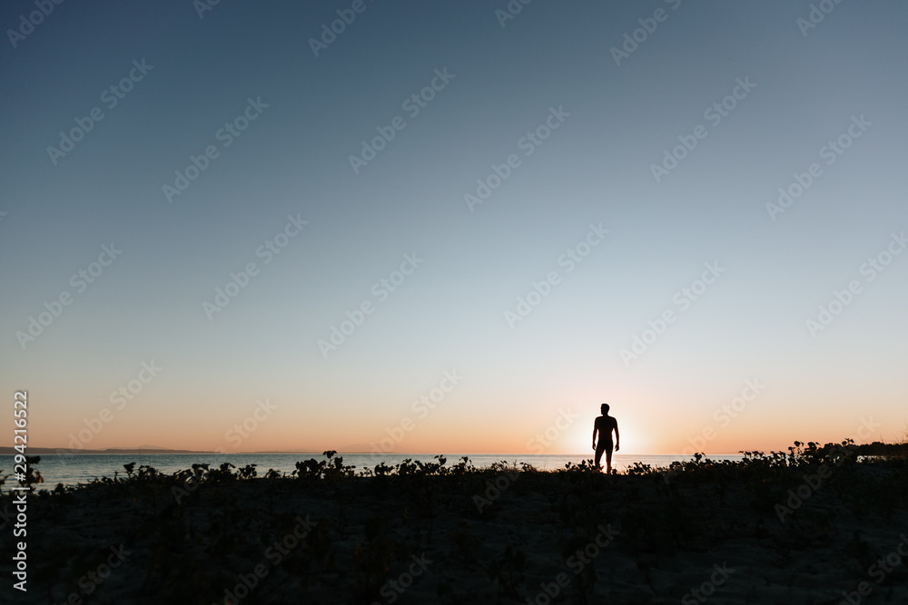 Silhouette of a young man enjoying beautiful sunset on the beach 