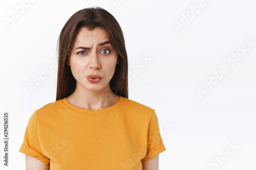 Ouch it probably hurts. Pity good-looking modern brunette woman in yellow t-shirt cringe and grimace as seeing someone got punched in face, folding lips and look uneasy camera, white background