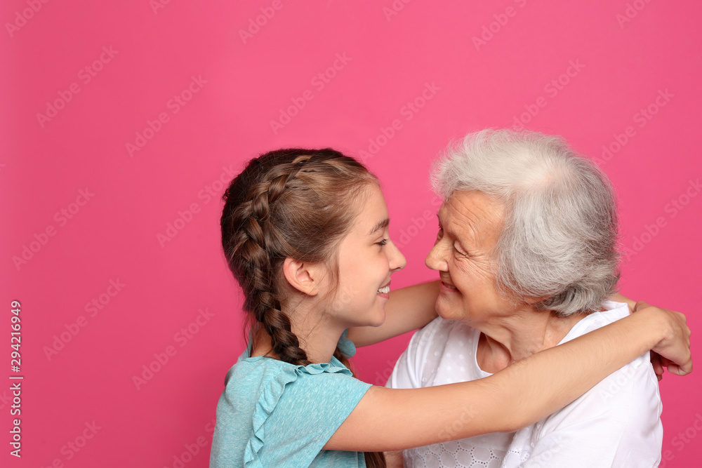Cute girl hugging her grandmother on pink background Cute girl hugging her grandmother on pink background