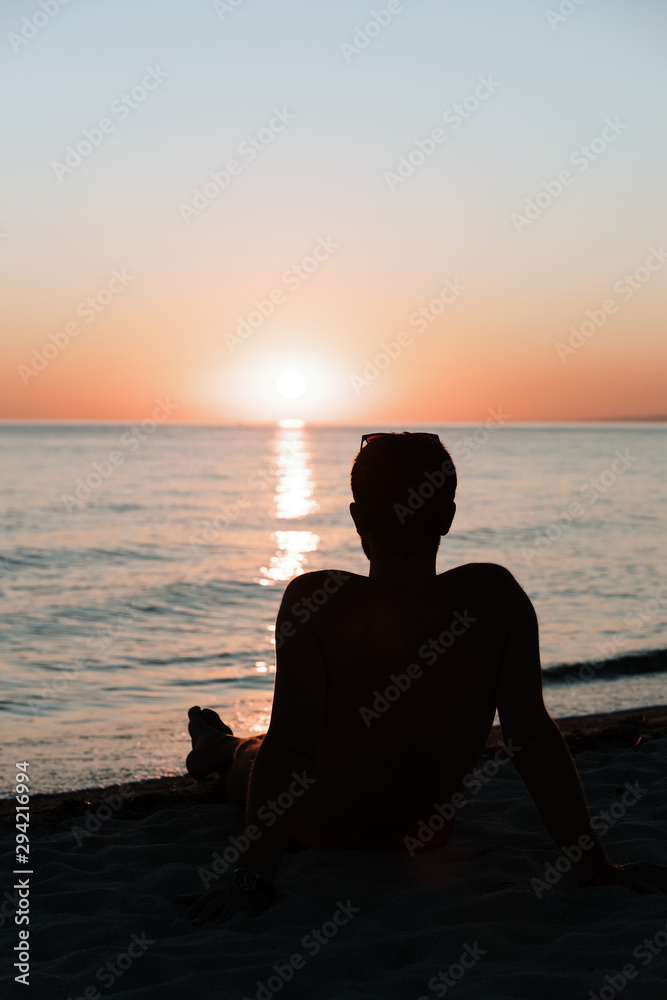 Silhouette of a young man enjoying beautiful sunset on the beach 