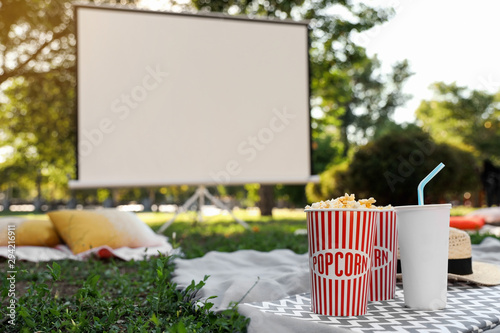 Fototapeta Naklejka Na Ścianę i Meble -  Popcorn and drink on green grass in open air cinema. Space for text