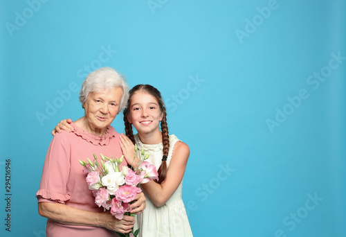 Cute girl and her grandmother with flowers on light blue background. Space for text