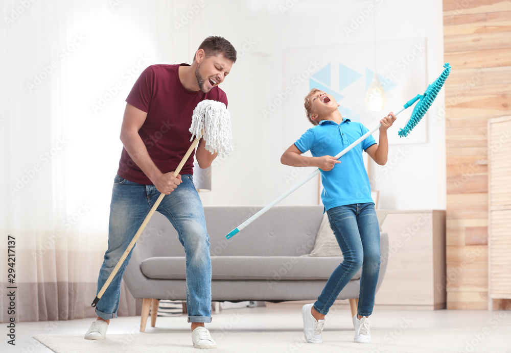 Dad and son having fun while cleaning living room together - obrazy, fototapety, plakaty 