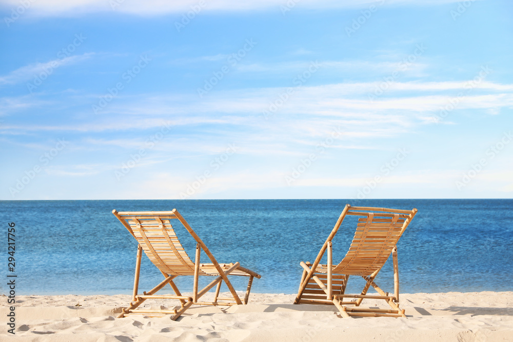 Wooden deck chairs on sandy beach near sea