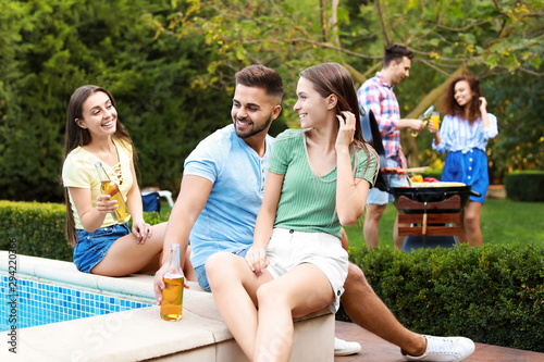 Happy friends with drinks at barbecue party near swimming pool outdoors