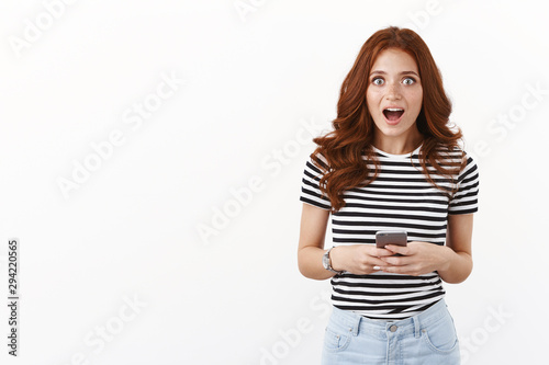 Omg have you seen her new post in social media. Impressed and shocked redhead girl gossiping about favorite actress after reading astonishing news in internet, hold smartphone, drop jaw surprised © Cookie Studio