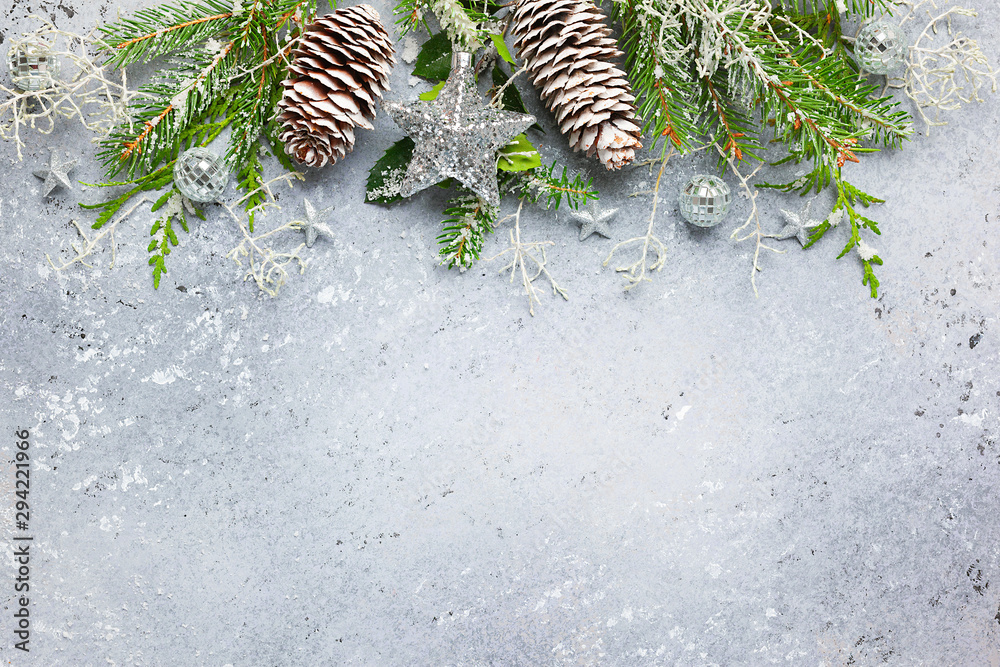 Naklejka Christmas or winter background with a border of green and frosted evergreen branches and pine cones on a grey vintage board. Flat lay