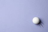 Golf ball flying on lilac background - creative image. Top view