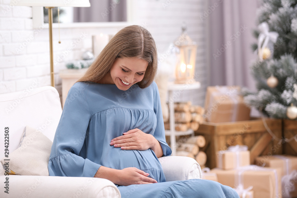 Young pregnant woman in room decorated for Christmas