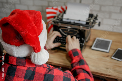 Modern Santa typing Merry Christmas greetings by vintage typewriter, typing machine. Santa Claus preparations for celebrating holiday
