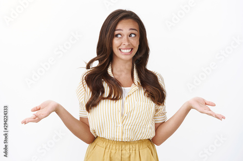 Oops, girl avoiding eye contact not to be caught on lying. Silly young girlfriend shrugging with hands spread sideways, smiling guilty look away, trying convince she has no idea what happened