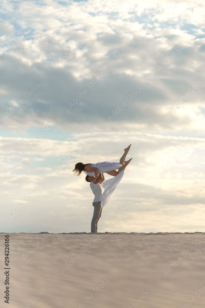 Romantic couple dancing in sand desert. The guy lifts the girl above himself. Sunset sky. Romantic couple dancing in sand desert. The guy lifts the girl above himself. Sunset sky.