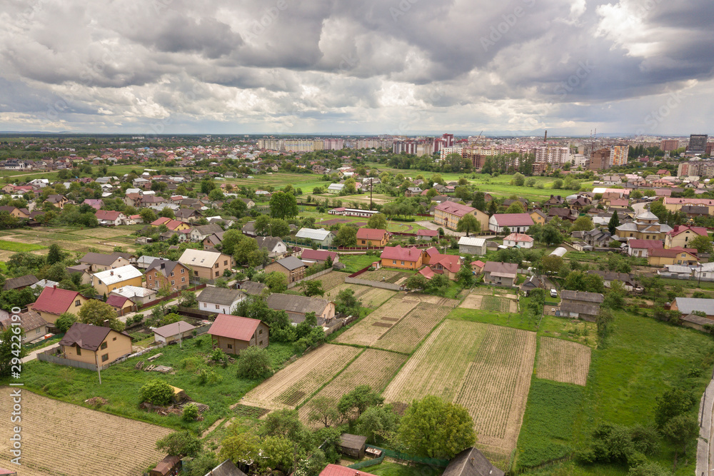 Aerial view of town or village with rows of buildings and curvy streets between green fields in summer. Countryside landscape from above.